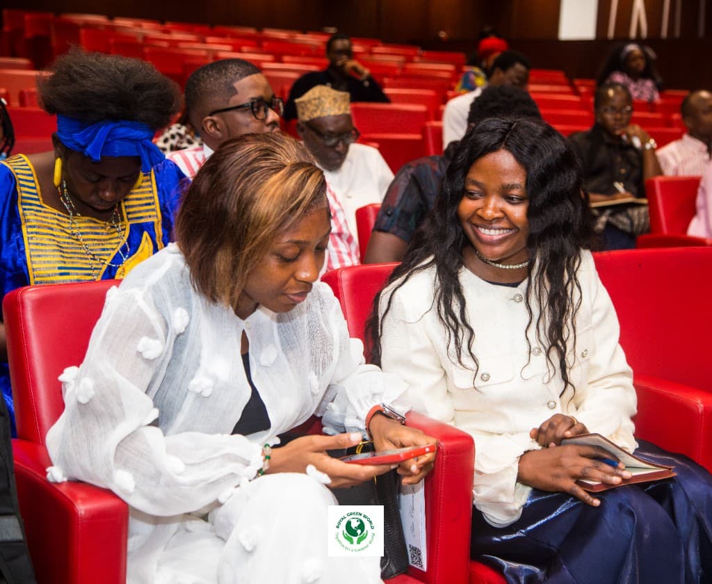 Two delegates seated together in the auditorium, one looking at a phone and the other holding a notebook